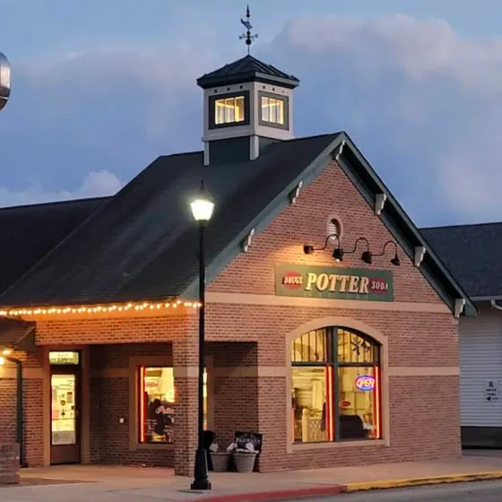 Brick building with a sign reading "Potter Soda," lit windows, and a streetlamp at dusk.