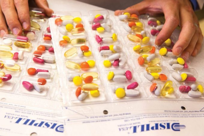 Hands organizing blister packs filled with various colorful pills on a table.