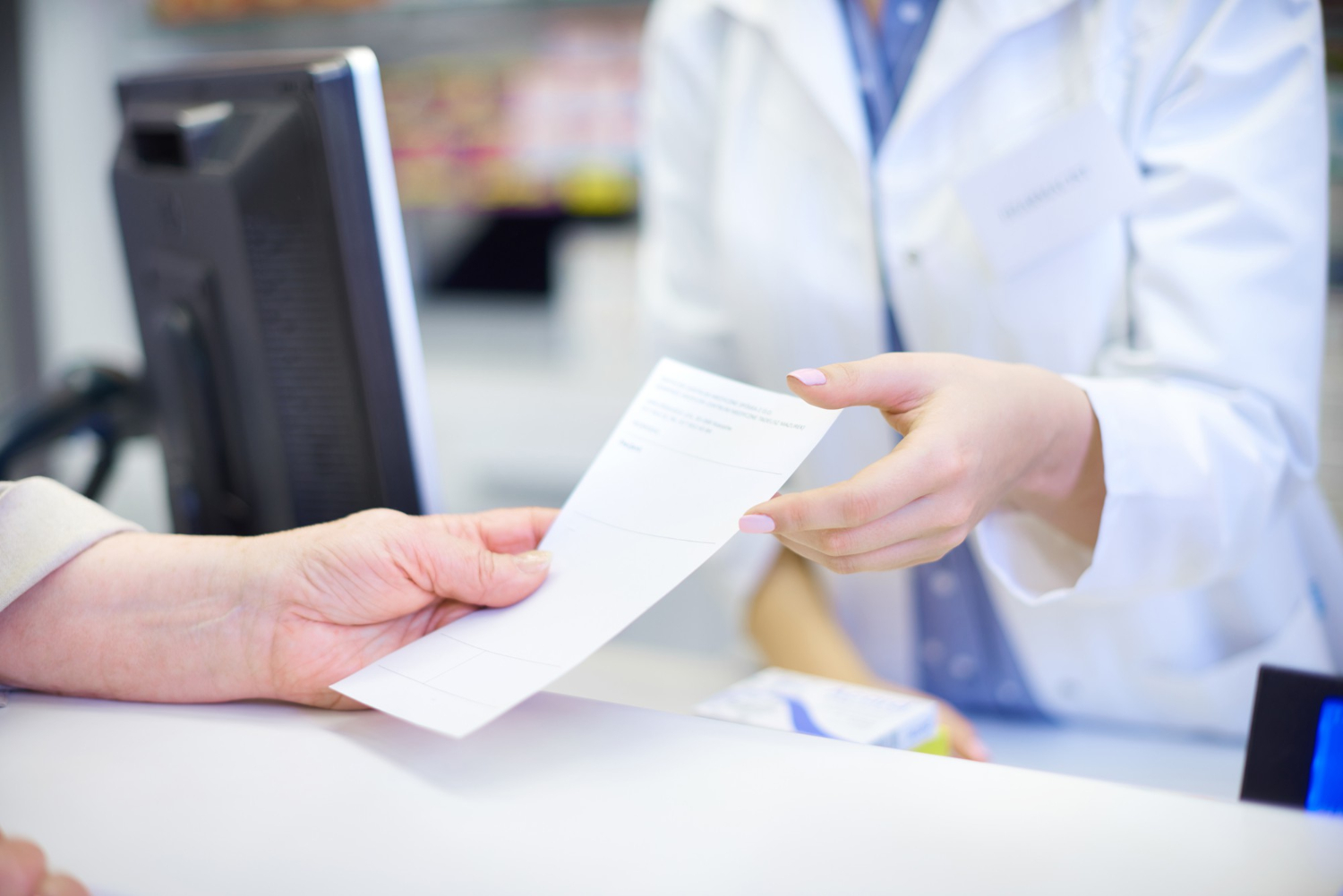 19485 Pharmacist handing a prescription paper to a customer across a pharmacy counter.